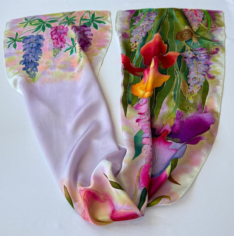 K&ouml;nnte beinhalten: Ein rechteckiger Seidenschal mit handgemaltem Blumenmuster. Ein Ende zeigt blaue, rosa und violette Lupinen auf einem zart lavendelfarbenen Hintergrund. Das andere Ende pr&auml;sentiert leuchtend orange, rote und violette Schwertlilien mit gr&uuml;nem Blattwerk.