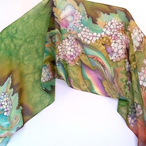 Puede incluir: Una bufanda de seda con un diseño floral que presenta hortensias en tonos de rosa, blanco y azul. El fondo es un degradado de verde, marrón y naranja.