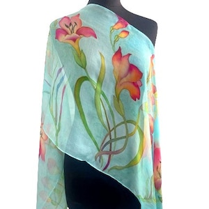 Pode incluir: Um len&ccedil;o leve e semitransparente com fundo turquesa claro e um padr&atilde;o floral pintado &agrave; m&atilde;o. O design apresenta flores vibrantes em tons de rosa e laranja, semelhantes a l&iacute;rios, com caules e folhas verdes longos, drapeado num manequim escuro.
