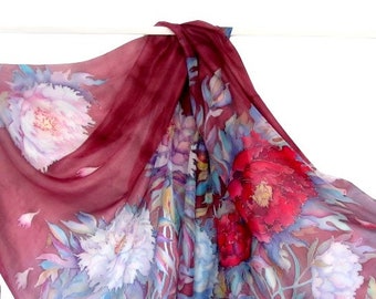 Puede incluir: Una bufanda de seda color burdeos con un patrón floral. Las flores están pintadas en tonos de rosa, blanco y azul. La bufanda está drapeada sobre una superficie blanca.
