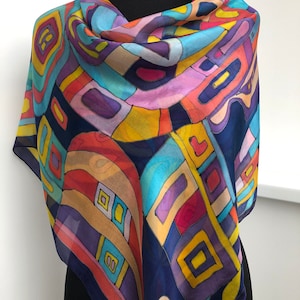 May include: A silk scarf with a colorful abstract geometric pattern on a dark blue background. The pattern includes yellow, red, orange, purple, blue, and green colors.