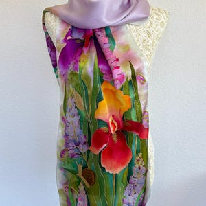 K&ouml;nnte beinhalten: Ein Seidenschal mit handgemaltem Blumenmuster, das leuchtend rote, orangefarbene und violette Schwertlilien, gr&uuml;nes Blattwerk und eine kleine braune Schnecke zeigt. Der Schal hat einen einfarbigen, hellvioletten oberen Teil und die Signatur Zamkova.