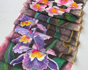 May include: A rectangular silk scarf featuring hand-painted floral motifs. The design displays vibrant pink and purple orchids with yellow centers, set against a dark, moody background with green foliage and stems throughout the fabric.