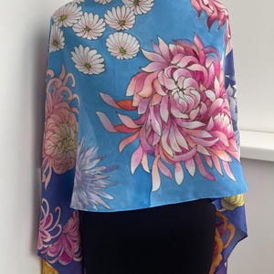 May include: A blue silk scarf with a floral print of pink, white, and yellow flowers. The scarf is draped over a black mannequin.