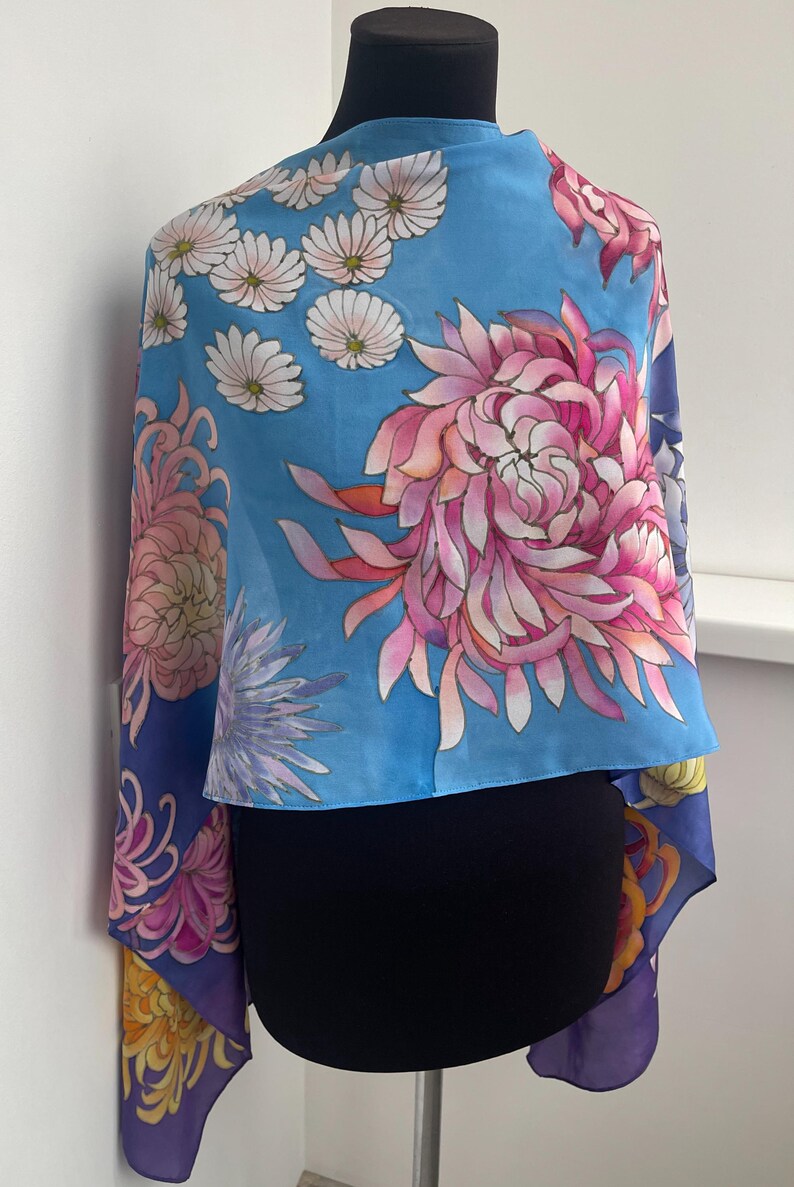 May include: A blue silk scarf with a floral print of pink, white, and yellow flowers. The scarf is draped over a black mannequin.
