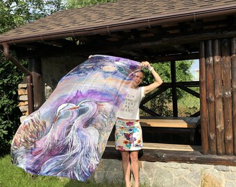 Puede incluir: Una mujer sostiene una bufanda de seda morada y azul con una pintura de acuarela de dos pájaros. La bufanda tiene un fondo blanco con un cielo azul claro y nubes. El texto "Calm and open my heart" está impreso en la camiseta blanca de la mujer.