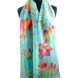 Pode incluir: Um len&ccedil;o leve com um padr&atilde;o floral vibrante com flores em tons de rosa, laranja e amarelo sobre um fundo azul turquesa suave. O design inclui caules e folhas verdes delicadas, criando um motivo bot&acirc;nico.