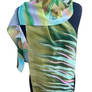 Puede incluir: Una bufanda de seda verde, azul y rosa con un dise&ntilde;o floral y abstracto. La bufanda est&aacute; doblada y drapeada sobre un maniqu&iacute;.