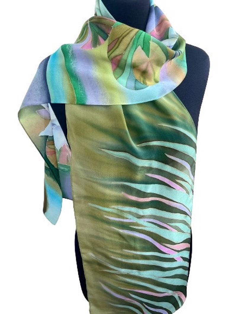 Puede incluir: Una bufanda de seda verde, azul y rosa con un dise&ntilde;o floral y abstracto. La bufanda est&aacute; doblada y drapeada sobre un maniqu&iacute;.
