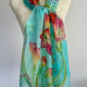 Pode incluir: Um len&ccedil;o leve com um fundo turquesa vibrante e motivos florais pintados &agrave; m&atilde;o em tons de rosa, laranja e amarelo. O design apresenta caules e folhas verdes alongadas que se entrela&ccedil;am pelo tecido, criando um padr&atilde;o bot&acirc;nico fluido.