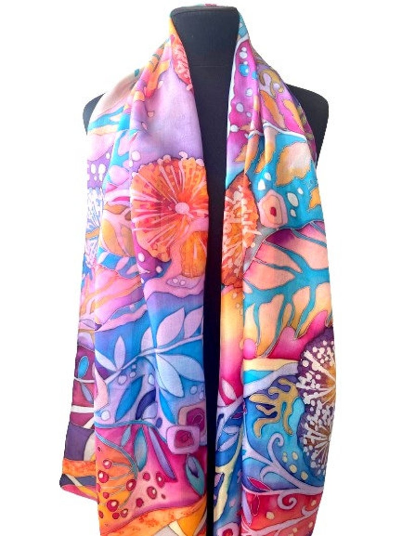 May include: A colorful silk scarf with a floral and abstract design. The scarf features shades of pink, orange, blue, and yellow.