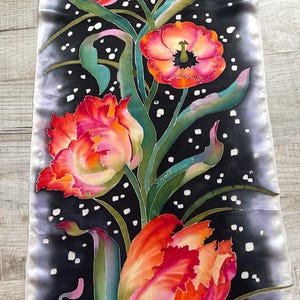Può includere: Un foulard di seta con sfondo nero e un bordo sfumato bianco. Il foulard presenta un disegno dipinto a mano di tulipani arancioni, rosa e gialli con foglie e steli verdi. Il disegno è cosparso di punti bianchi. La firma dell'artista, "Zamkova T", è visibile nell'angolo in basso a destra.