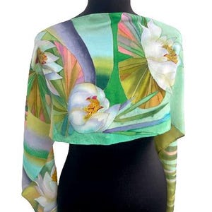 Puede incluir: Una bufanda de seda verde con un dise&ntilde;o floral con flores blancas y hojas verdes. La bufanda tiene un degradado de azul claro y rosa en el fondo.
