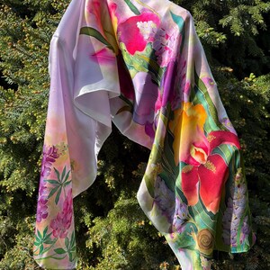 K&ouml;nnte beinhalten: Ein leichtes Tuch mit einem lebendigen Blumenmuster aus gro&szlig;en roten, gelben und violetten Bl&uuml;ten, gr&uuml;nen Bl&auml;ttern und einer kleinen Schneckenillustration. Der Stoff hat eine glatte, flie&szlig;ende Textur mit wei&szlig;em Hintergrund und bunten Motiven.