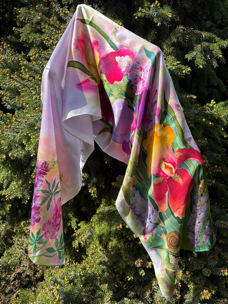 K&ouml;nnte beinhalten: Ein leichtes Tuch mit einem lebendigen Blumenmuster aus gro&szlig;en roten, gelben und violetten Bl&uuml;ten, gr&uuml;nen Bl&auml;ttern und einer kleinen Schneckenillustration. Der Stoff hat eine glatte, flie&szlig;ende Textur mit wei&szlig;em Hintergrund und bunten Motiven.