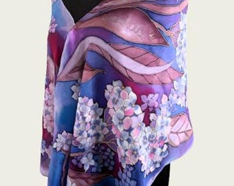 May include: A silk scarf with a floral design in shades of blue, purple, and pink. The scarf features a watercolor-style painting of hydrangeas and leaves. The scarf is draped over a black mannequin.