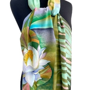 Puede incluir: Una bufanda de seda verde, azul y blanca con un dise&ntilde;o pintado a mano de un nen&uacute;far. La bufanda tiene un patr&oacute;n de rayas en un lado y un patr&oacute;n floral en el otro.