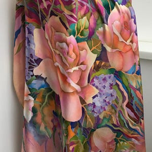 May include: A silk scarf featuring a hand-painted floral pattern with large peach-colored roses, clusters of small purple flowers, and green foliage. The background transitions between shades of soft pink, deep magenta, and violet, creating a vibrant, multi-colored botanical design on the fabric.