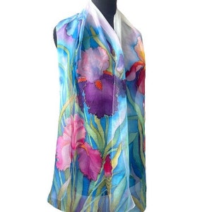 May include: A lightweight scarf featuring a hand-painted floral design of purple, pink, and deep red iris flowers set against a vibrant blue background with long green stems and leaves, displayed on a black mannequin torso for clear visibility.