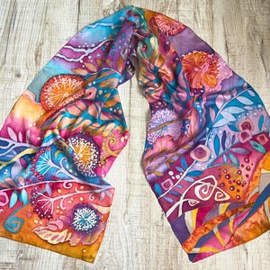 May include: A colorful silk scarf with a floral pattern in shades of pink, orange, blue, and purple. The scarf features a variety of flowers and leaves, and the background is a light blue.