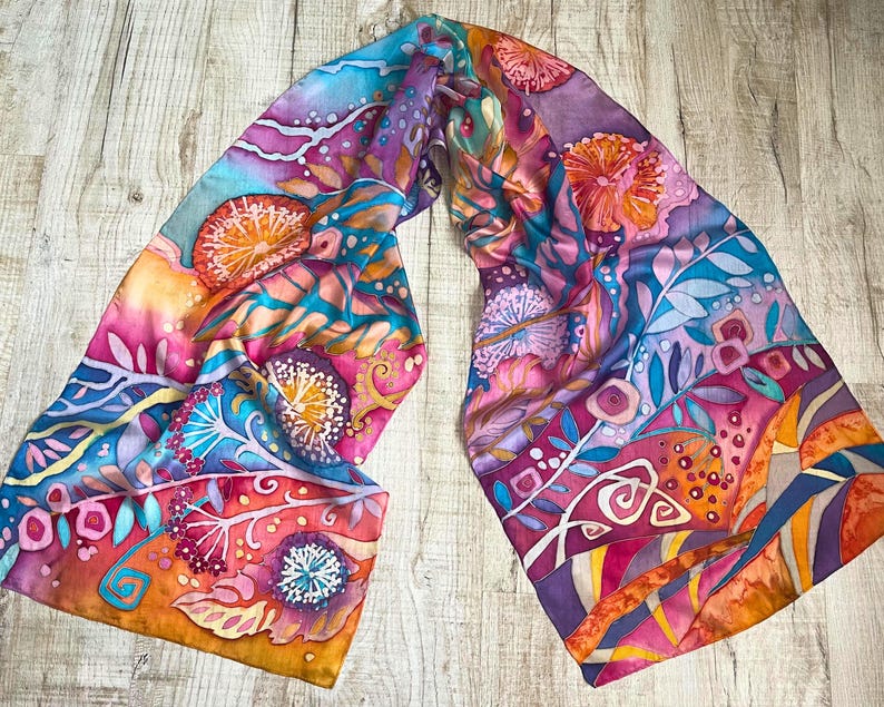 May include: A colorful silk scarf with a floral pattern in shades of pink, orange, blue, and purple. The scarf features a variety of flowers and leaves, and the background is a light blue.