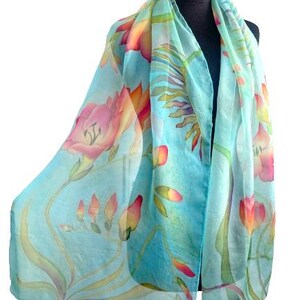 Pode incluir: Um len&ccedil;o leve e semitransparente num tom azul-claro vibrante, com um padr&atilde;o floral pintado &agrave; m&atilde;o que apresenta flores delicadas em rosa e laranja, caules verdes e folhagem que se espalha pelo tecido num estilo semelhante a aguarela.