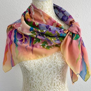 May include: A square silk scarf featuring a hand-painted design with a vibrant color palette of pink, purple, blue, and green. The pattern includes abstract flowing shapes and organic leaf-like motifs with defined outlines, draped around a mannequin.