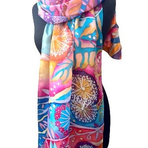 May include: A colorful silk scarf with a floral pattern in shades of pink, orange, blue, and yellow. The scarf features a repeating design of stylized flowers and leaves.