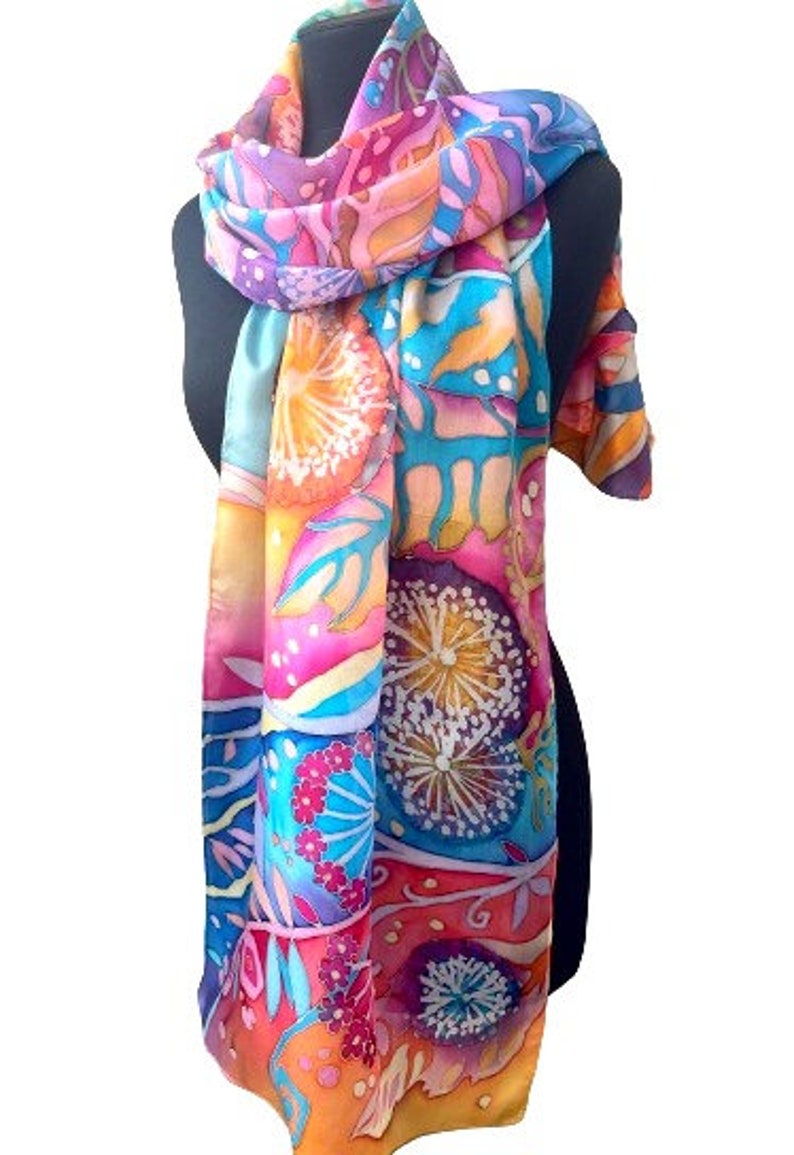 May include: A colorful silk scarf with a floral pattern in shades of pink, orange, blue, and yellow. The scarf features a repeating design of stylized flowers and leaves.