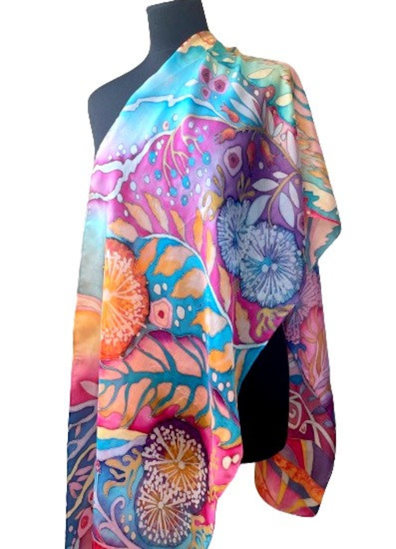 May include: A colorful silk scarf with a floral pattern in shades of pink, blue, yellow, and orange. The scarf features a variety of flowers and leaves, and the design is reminiscent of a garden.