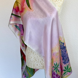 K&ouml;nnte beinhalten: Ein quadratischer Seidenschal mit einem sanften lavendelfarbenen Zentrum und einem lebendigen Blumenrand. Das Design zeigt handgemalte Illustrationen von violetten Lupinen, gr&uuml;nen Bl&auml;ttern und rosa Bl&uuml;ten auf einem hellen, pastellfarbenen Hintergrund.