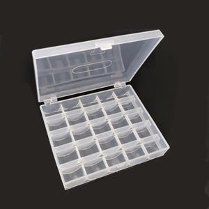 May include: A clear plastic storage box with a hinged lid, divided into 25 small square compartments. The lid is partially open, revealing the interior. The box is designed for organizing small items like beads or jewelry findings.
