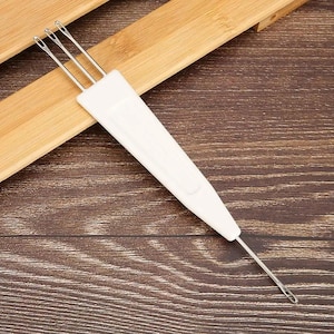 Op de afbeelding: Een witte latch hook tool met drie naalden en een lange handgreep. De tool is ontworpen voor tapijthaken en andere vezelambachten. De handgreep is gemaakt van wit plastic.