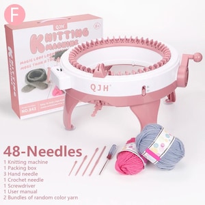 Op de afbeelding: Een ronde roze en witte breimachine met 48 naalden, een handzwengel en een doos met het label QJH Knitting Machine. Inbegrepen zijn drie handnaalden, één haaknaald, één schroevendraaier en twee bundels garen in roze en grijs.