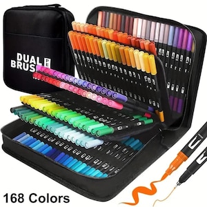Puede incluir: Un estuche de transporte negro con cremallera que contiene 168 rotuladores de doble punta en un amplio espectro de colores. El estuche presenta el texto DUAL BRUSH PEN en la parte frontal. Los rotuladores están organizados en ranuras escalonadas, mostrando tonos de rojo, naranja, amarillo, verde, azul y morado.