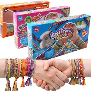 Może przedstawiać: Trzy prostokątne kartonowe pudełka na zestawy biżuterii Best Friend Bands w kolorze pomarańczowym, różowym i niebieskim, z obrazkami kolorowych plecionych bransoletek. Poniżej widać dwa nadgarstki z wieloma żywymi, wielokolorowymi plecionymi bransoletkami.