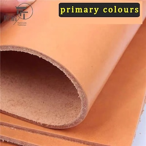 Peut inclure: Une pièce de cuir tanné végétal de couleur beige, épaisse, pliée pour révéler un grain supérieur lisse et un envers fibreux semblable à du daim. La surface est de couleur uniforme. Une étiquette noire affiche le texte primary colours.