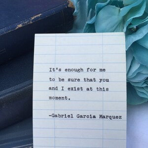 May include: A white card with blue lines on it, featuring a quote by Gabriel Garcia Marquez: "It's enough for me to be sure that you and I exist at this moment."