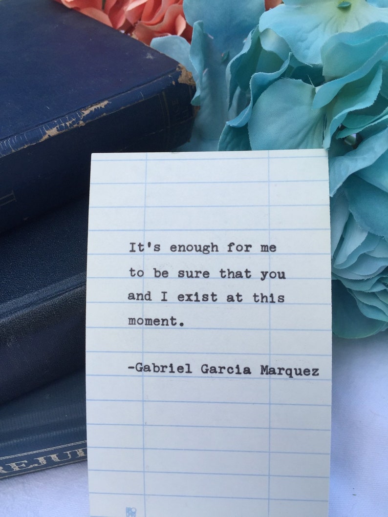 May include: A white card with blue lines on it, featuring a quote by Gabriel Garcia Marquez: "It's enough for me to be sure that you and I exist at this moment."