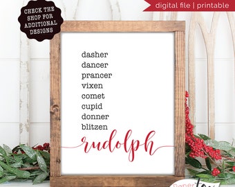May include: A framed white print with a list of reindeer names in black text, with "Rudolph" in red script. The frame is made of wood. The top right corner has the text "digital file | printable".