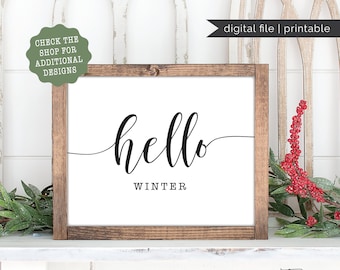 May include: A framed white sign with the words "hello WINTER" in black script and block letters. The frame is made of dark wood. The sign is decorated with greenery and red berries. The words "digital file | printable" are in the upper right corner.