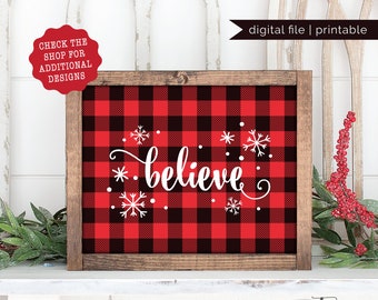 May include: A framed sign with a red and black buffalo plaid pattern. The word "believe" is written in white script with snowflakes. The sign is a digital file and printable.
