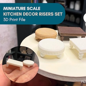 May include: A collection of miniature kitchen decor risers, featuring a round beige riser, a square white riser, and a small brown table. The image includes the text "MINIATURE SCALE KITCHEN DECOR RISERS SET 3D Print File".