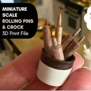 May include: A miniature set of rolling pins in a crock, a 3D print file. The crock is white with a brown rim, holding several brown rolling pins. A second white crock with white rolling pins is in the background. Text reads "MINIATURE SCALE ROLLING PINS & CROCK 3D Print File".