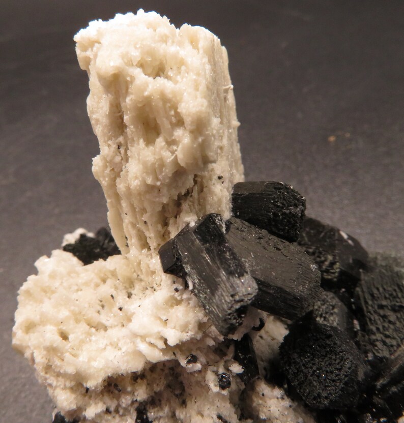 May include: A cluster of white and black crystals. The white crystals are tall and slender, while the black crystals are shorter and more blocky.