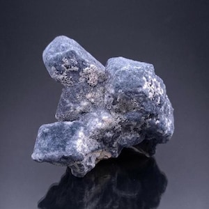 May include: A close-up of a blue mineral specimen with a rough, textured surface. The mineral has a crystalline structure and is a mix of blue and white hues. The specimen is displayed against a dark background.