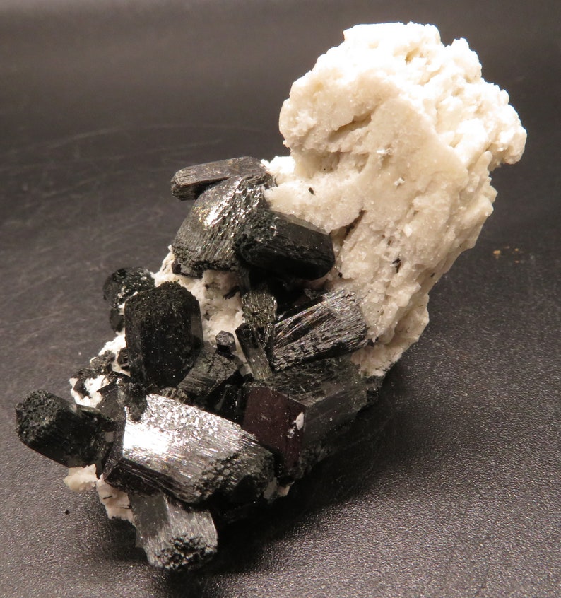 May include: A cluster of black, shiny, elongated crystals on a white, rough, mineral matrix.
