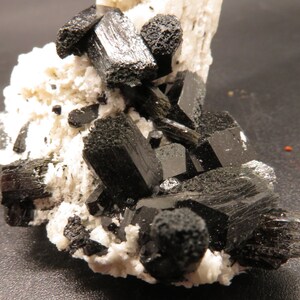 May include: A cluster of black schorl crystals on a white albite matrix. The crystals are sharp and well-formed, with a glassy luster.