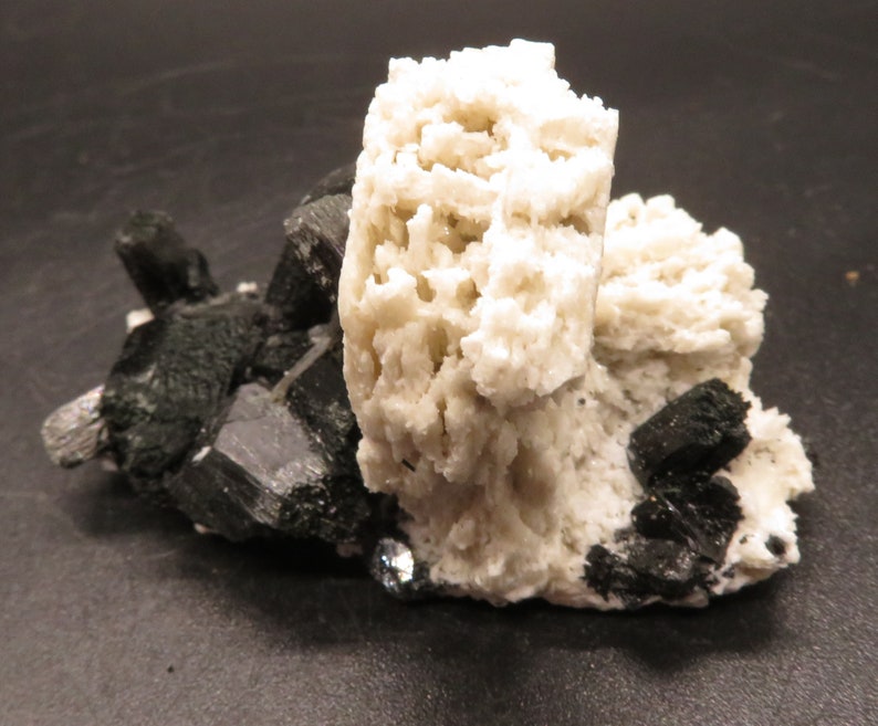 May include: A cluster of white, spiky crystals with black, shiny crystals growing around them. The white crystals are clustered together in a rounded shape, while the black crystals are more spread out.