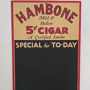 May include: Vintage "Hambone" cigar sign with red and black text on a tan background. The sign reads "Mild & Mellow 5¢ CIGAR A Certified Smoke SPECIAL for TO-DAY". The sign has a red border and a black section for additional text.
